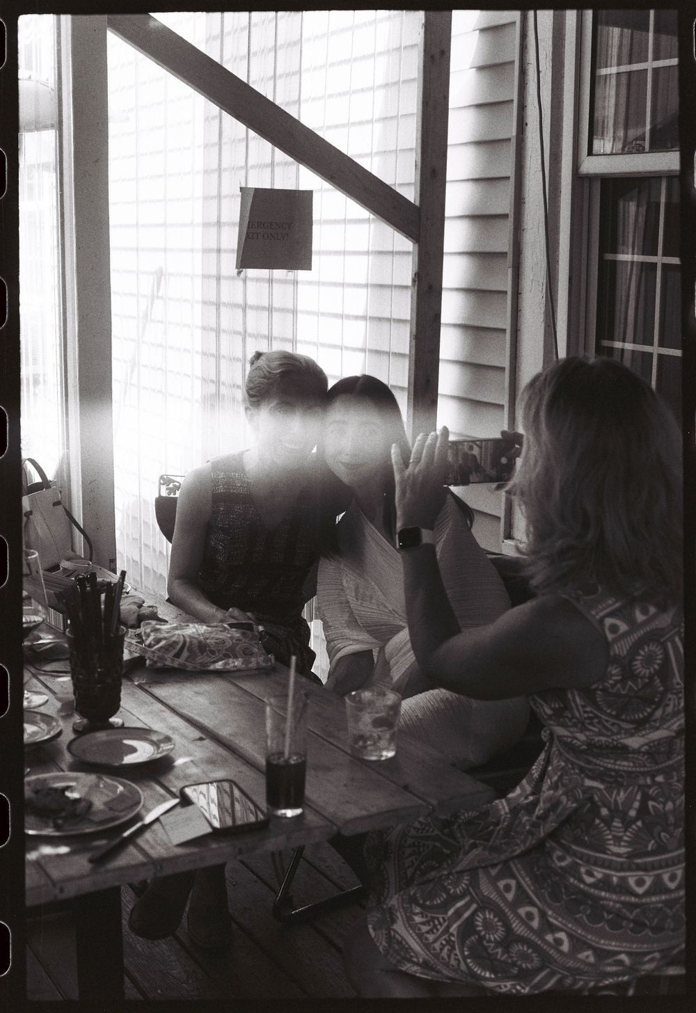 A black and white photo of a woman taking a photo with her phone of two friends smiling together on 35mm film in Brunswick, Maine.