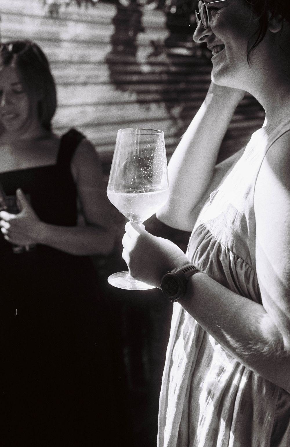 A detail photo of a guest at an engagement party holding a glass of wine in the sunshine on black and white film.