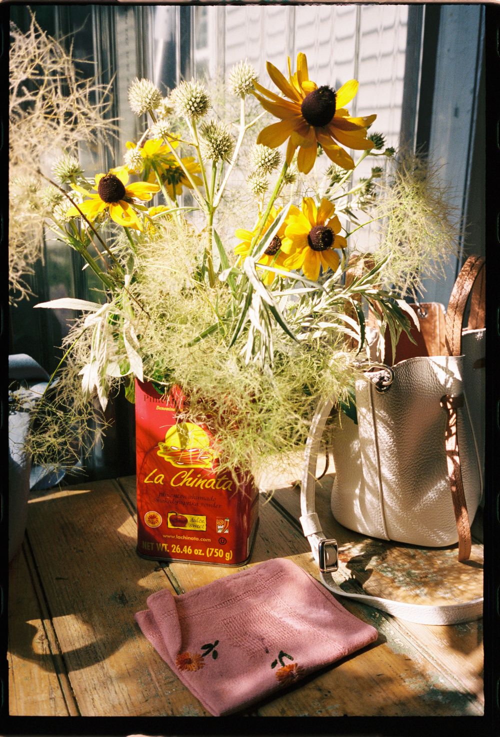 Flowers in a vintage coffee tin and purses and colorful napkins on the table in the sunshine during a bridal shower.