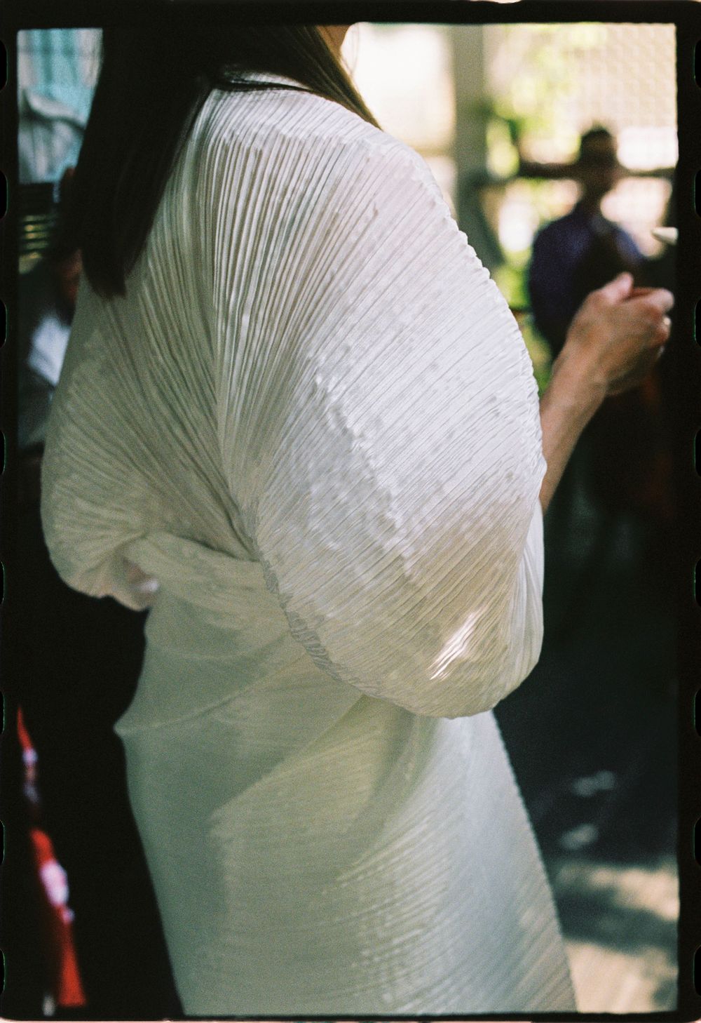 A detail photo of the bride to be's dress designed by Issey Miyake of his Pleats Please collection at a wine bar during a summer celebration