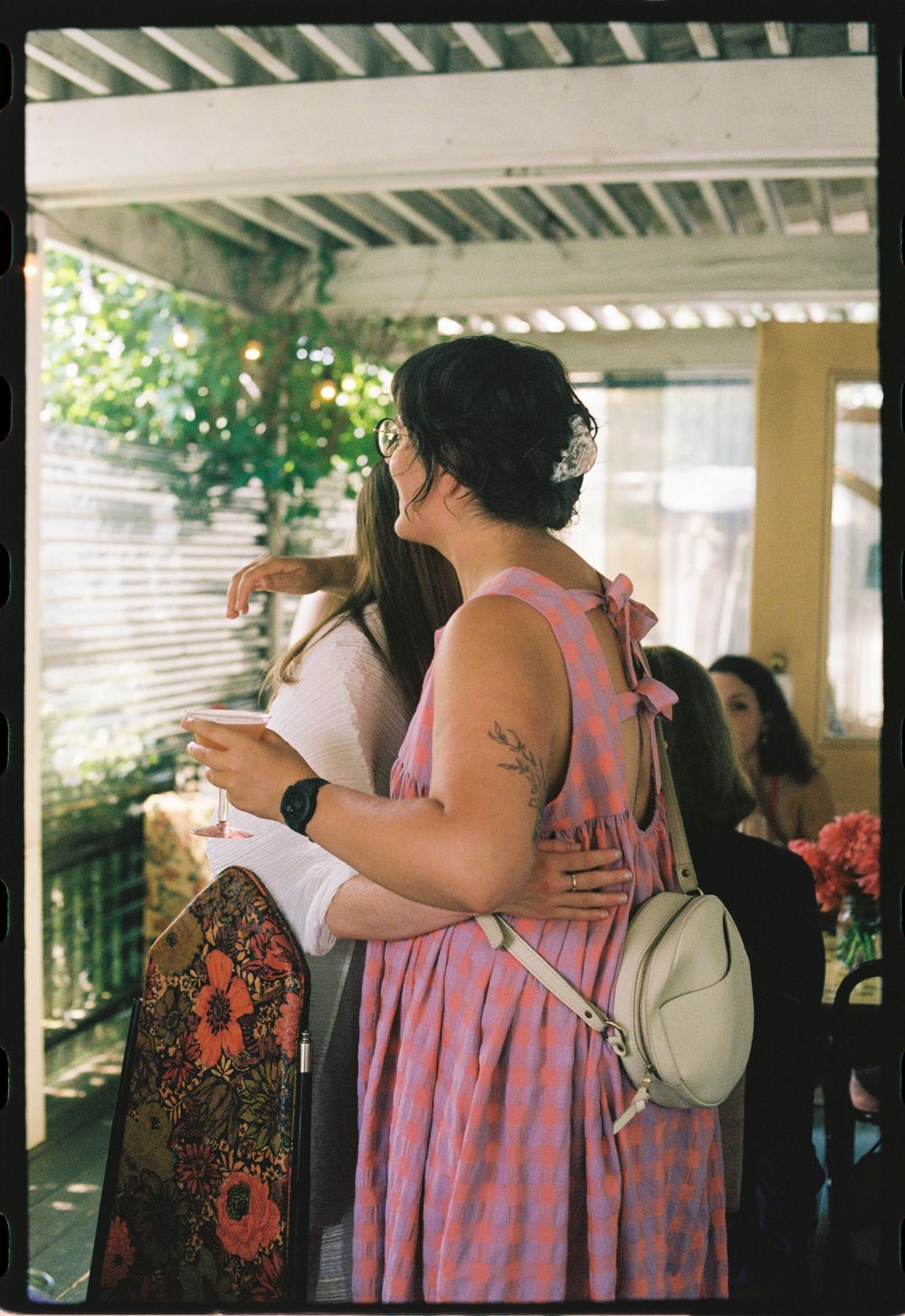 The bride to be embraces her friend in pink dress, glass in hand during a summer's celebration of their engagement in Maine.