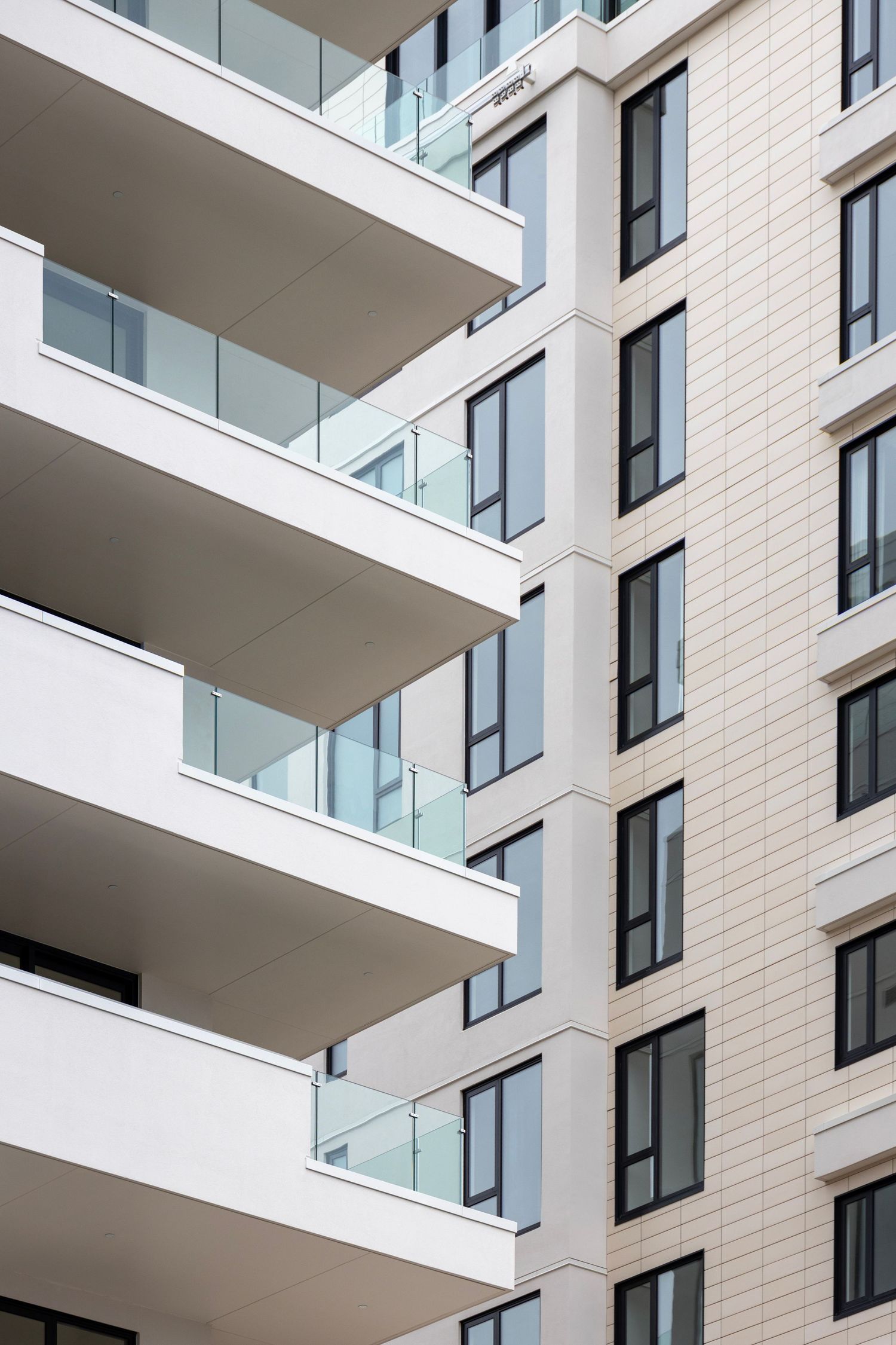White modern apartment building with clean horizontal balconies and transparent glass balustrades.