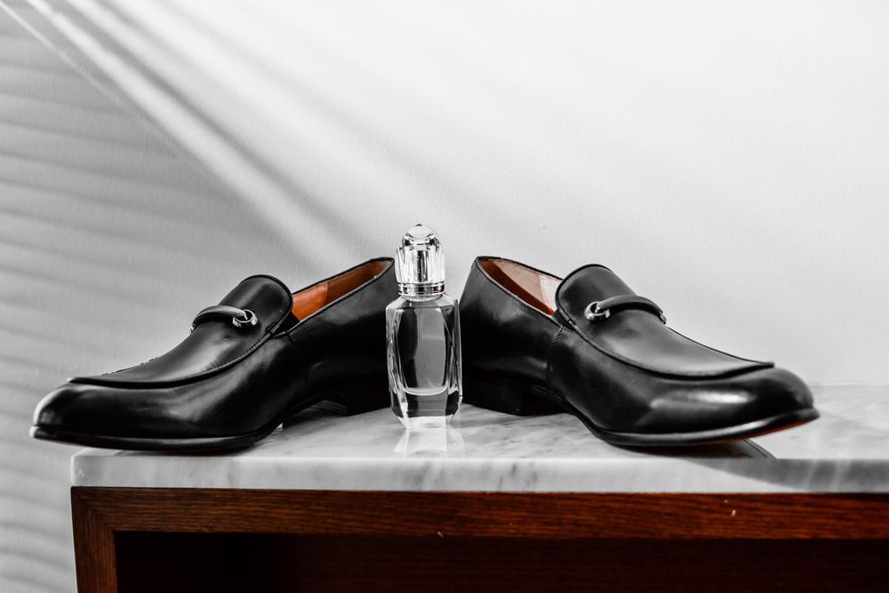 Elegant black leather dress shoes with silver perfume bottle displayed on wooden surface.