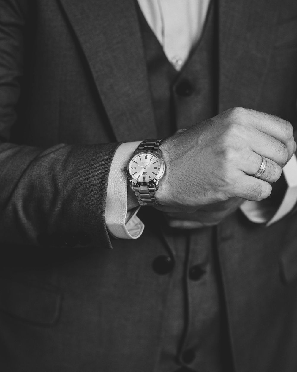 Close-up of groom's wrist showing watch and wedding ring against dark suit.