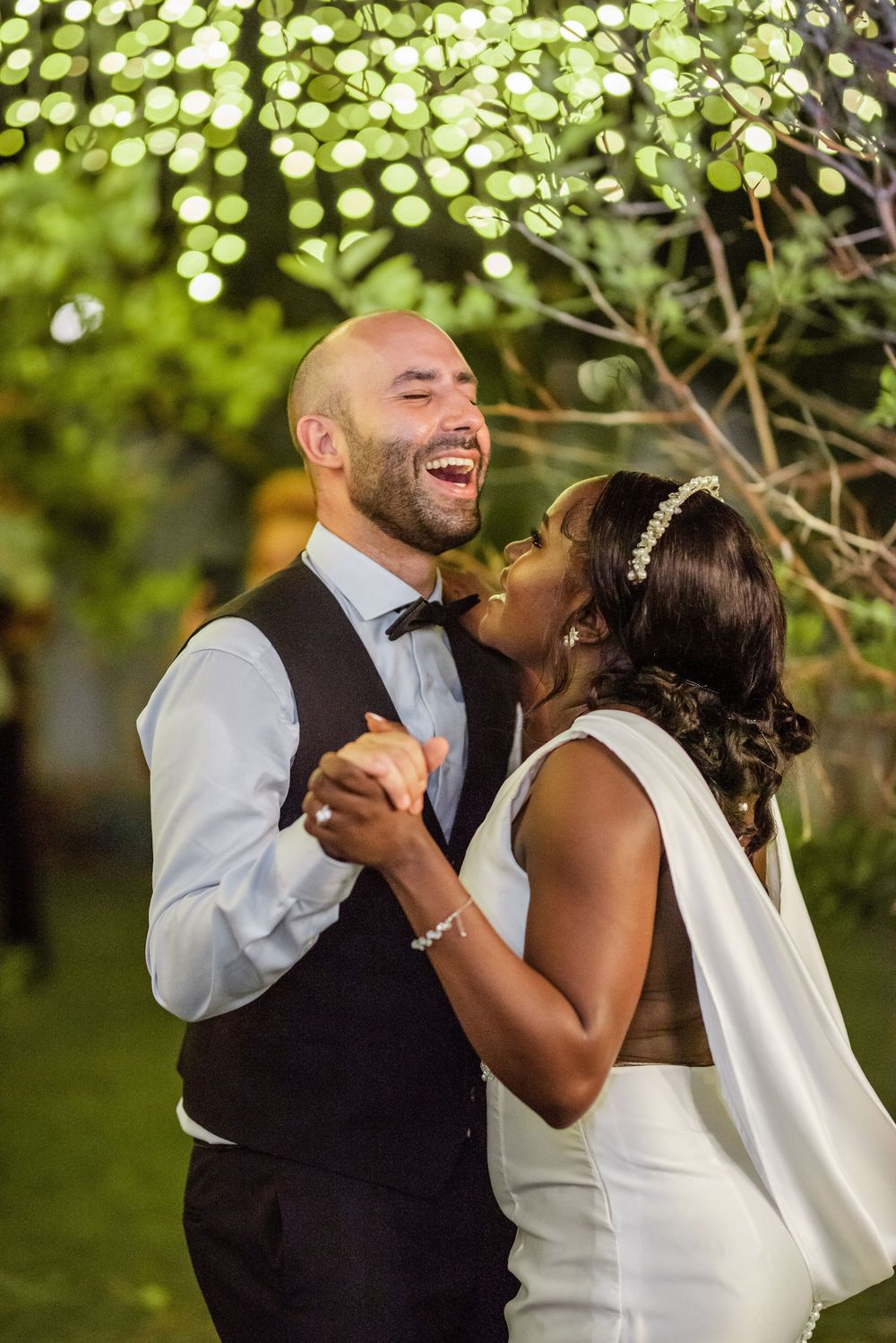 A couple shares an intimate dance moment under twinkling outdoor lights at their wedding reception.