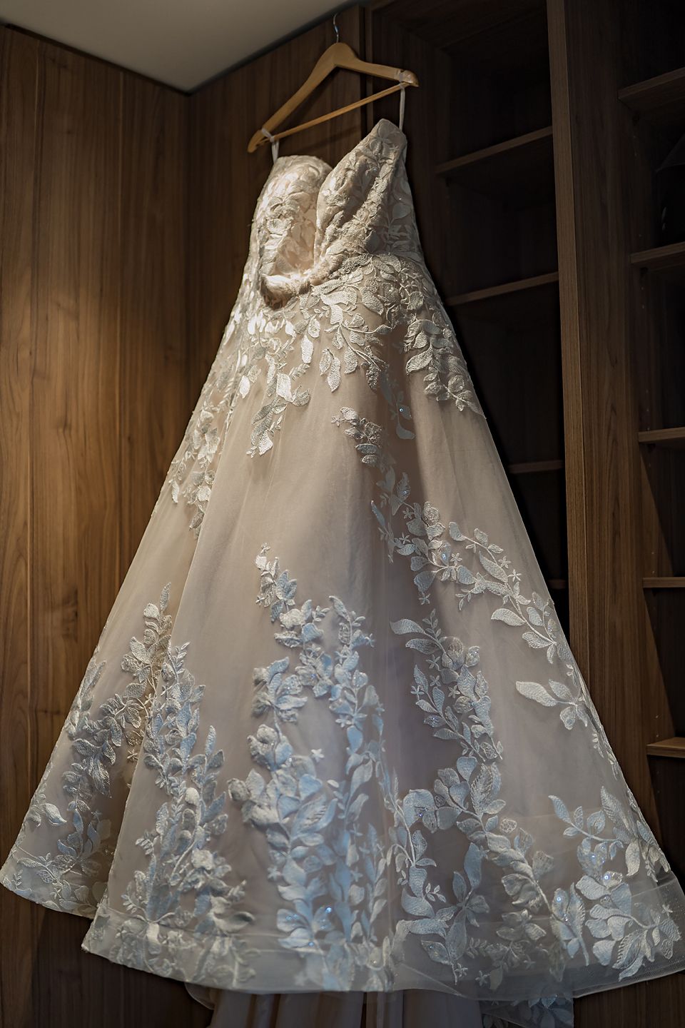 Elegant white wedding dress with lace detailing hanging on wooden hanger.