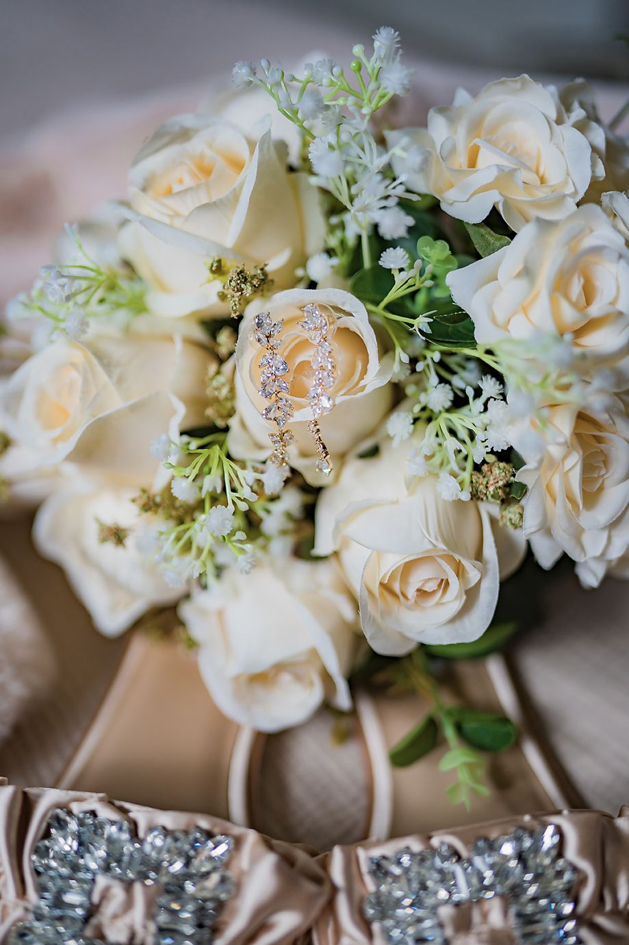 Elegant bouquet of cream-colored roses and delicate white flowers arranged with greenery and silver accents.
