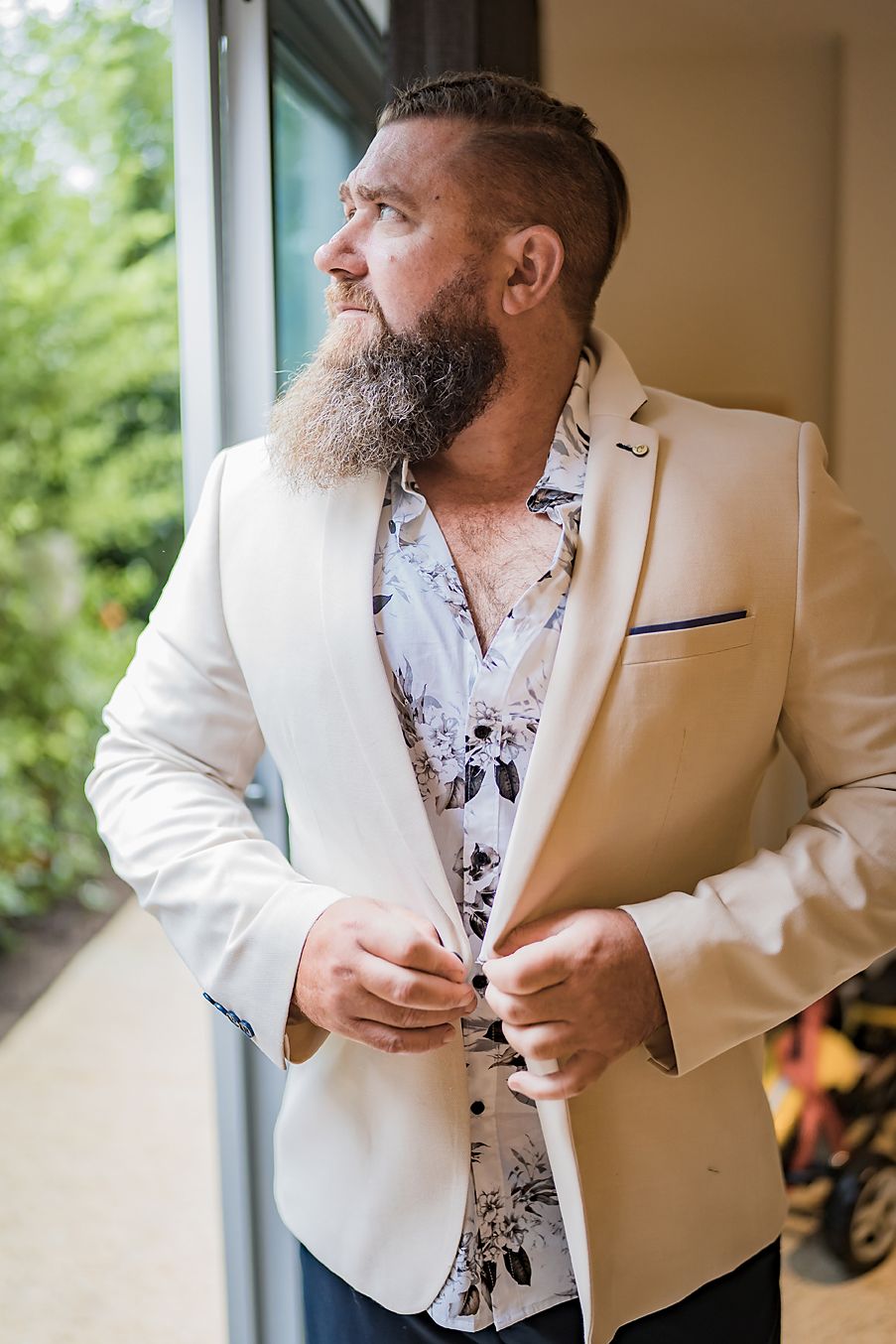 Close-up of formal white suit jacket being adjusted near a window with natural lighting.