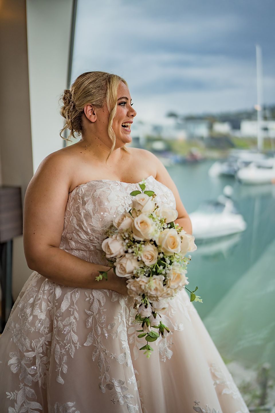 Elegant strapless lace wedding gown with floral details photographed by a marina with boats in background.