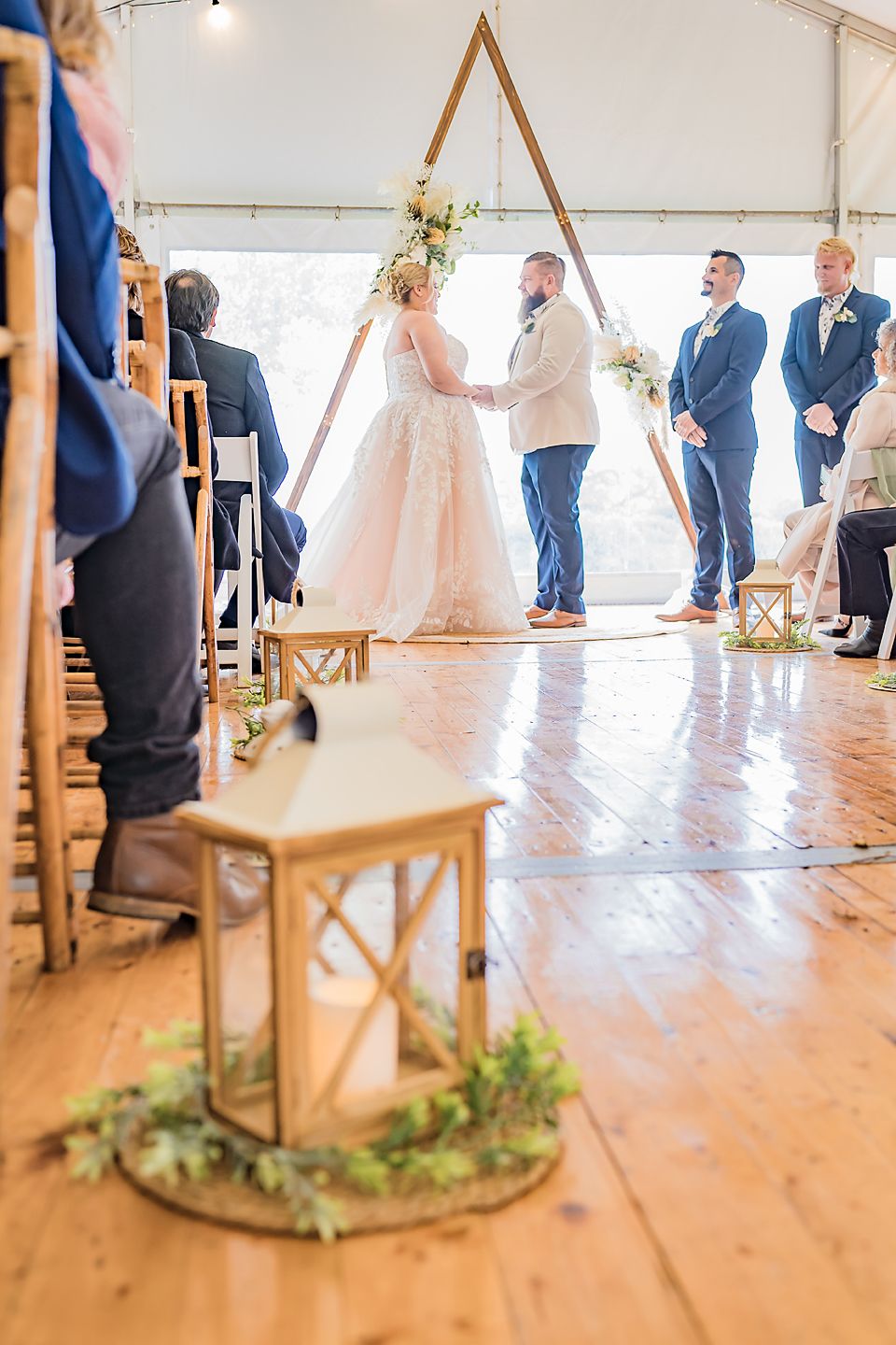 Indoor wedding ceremony space with wooden chairs and natural decor under a tent canopy.