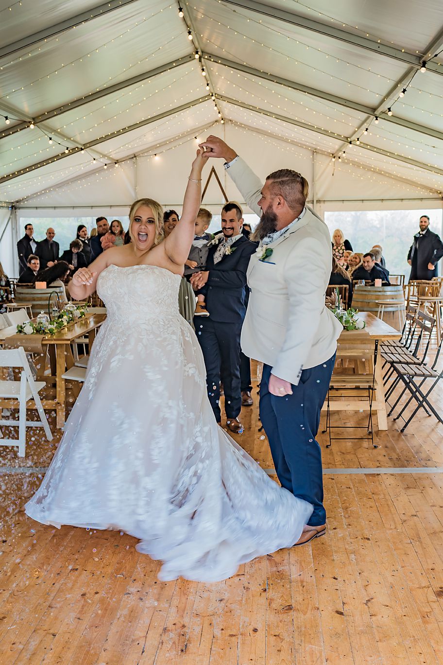 Wedding celebration in a tent with decorated wooden floor and string lights.