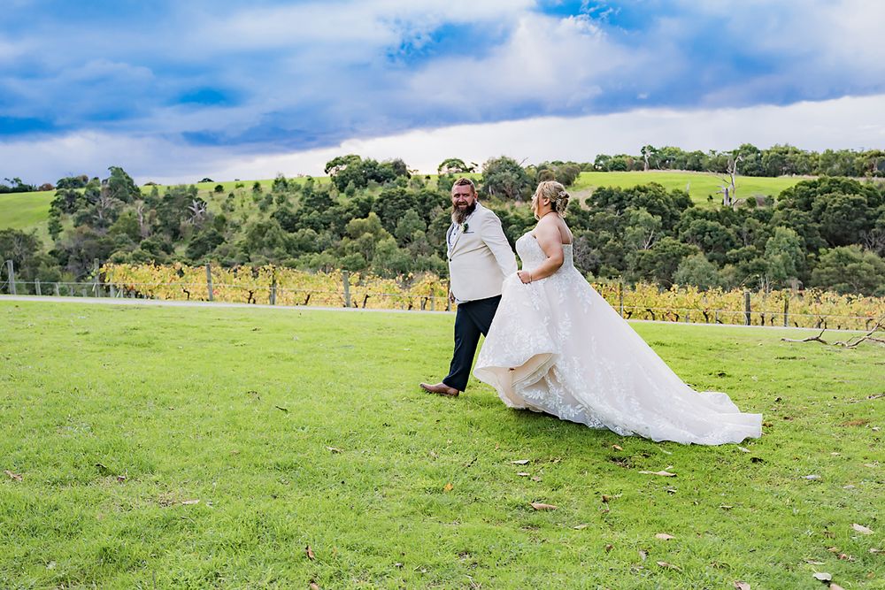 A couple walking on lush green grass with rolling hills in the background on a sunny day.