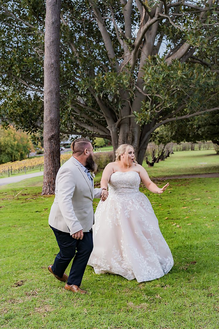 Wedding couple dancing on grass with trees in background.