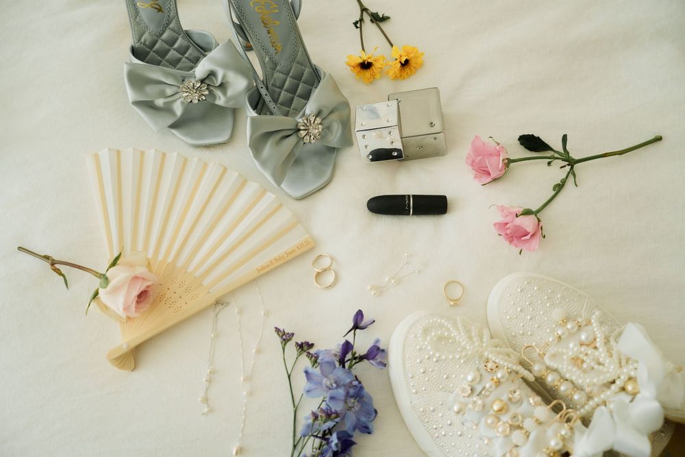Wedding detail flatlay with delicate paper fan, flowers, and accessories on light fabric.