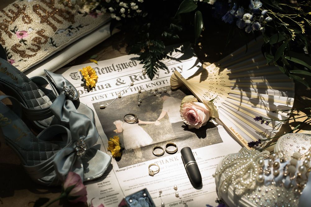 Artistic wedding detail photo with rings, flowers and paper in dramatic lighting.