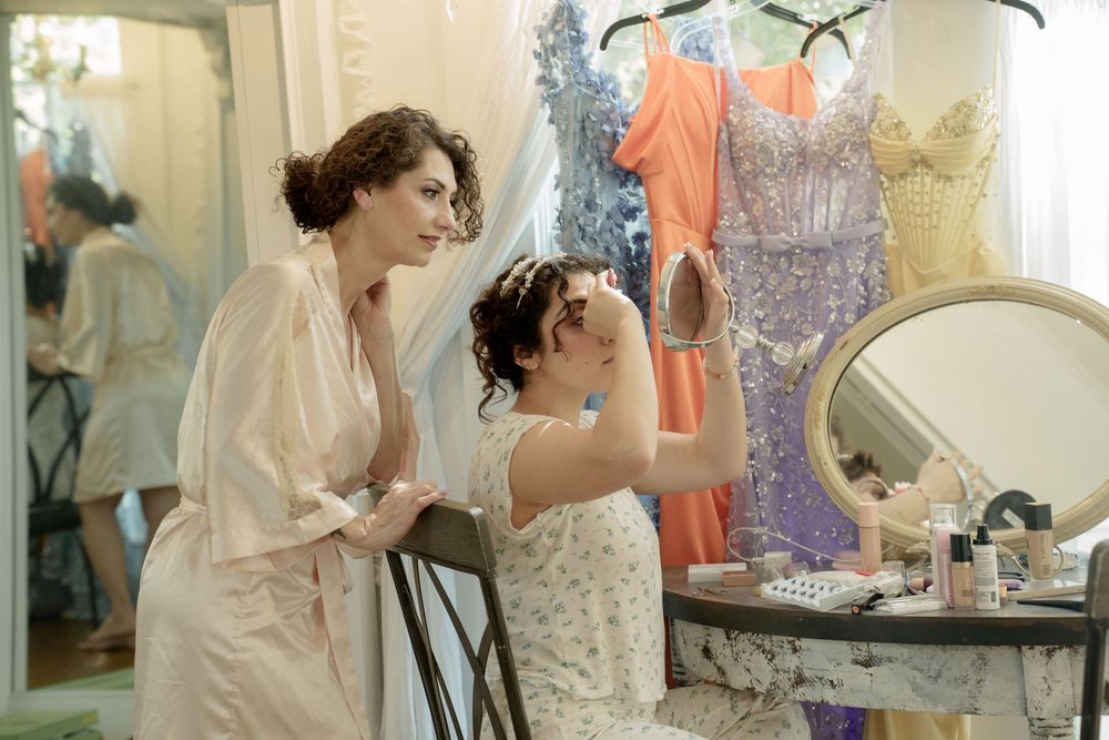 Bridesmaids getting ready in a bright white dressing room with mirrors and clothing racks.