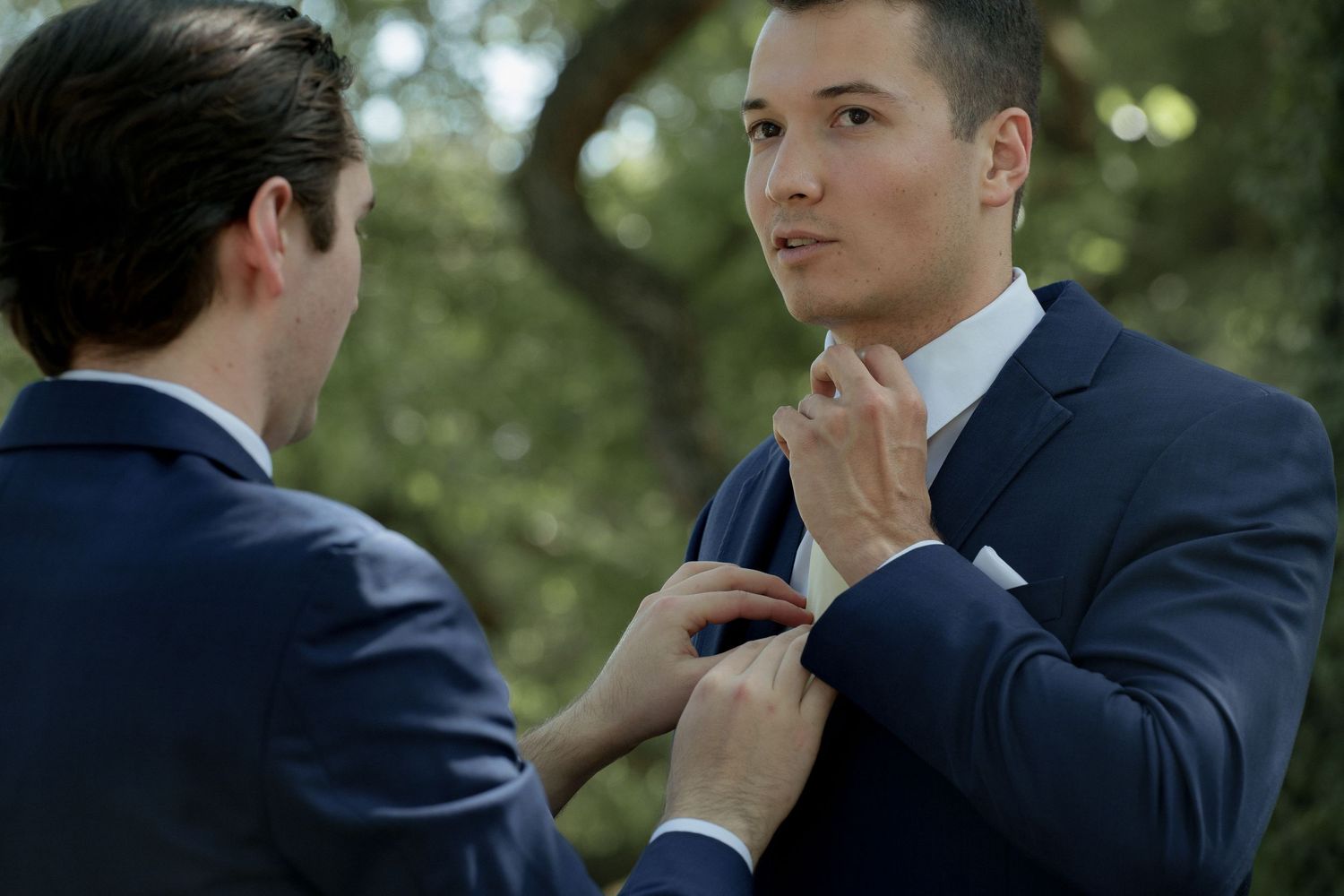 Groomsmen in navy suits adjusting ties outdoors.