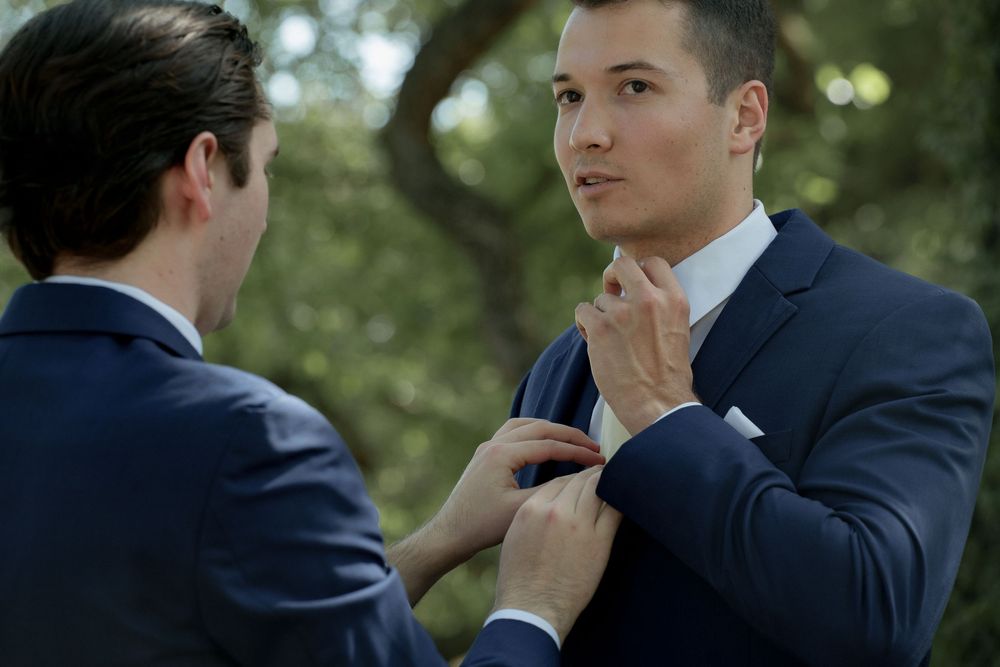 Groomsmen in navy suits adjusting ties outdoors.