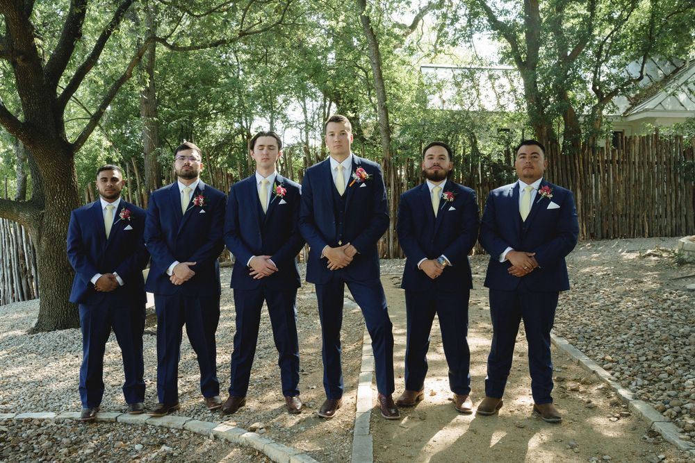 Groomsmen in navy suits and brown shoes lined up under trees.