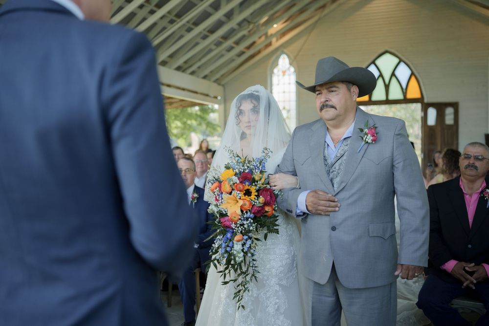 Wedding ceremony in progress with officiant in grey suit and cowboy hat.
