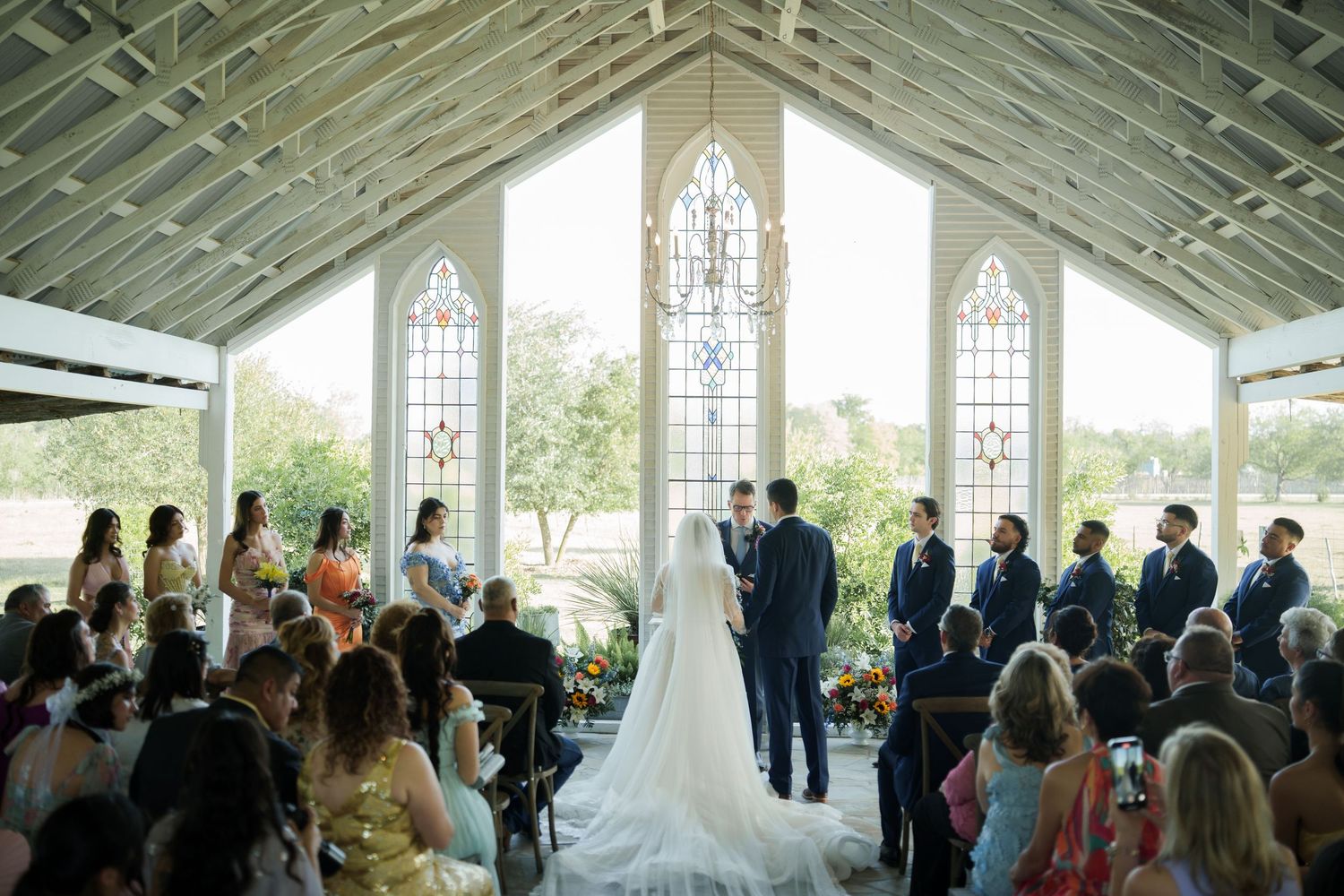 Wedding ceremony in a bright chapel with stained glass windows and gathered guests.
