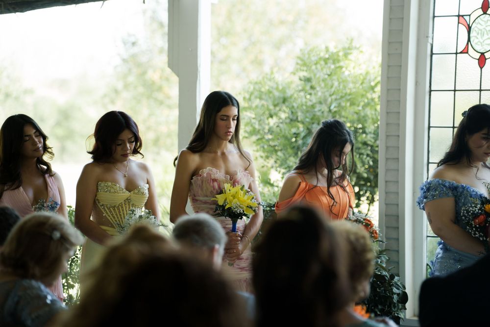 Bridesmaids in pastel dresses stand together during wedding ceremony.