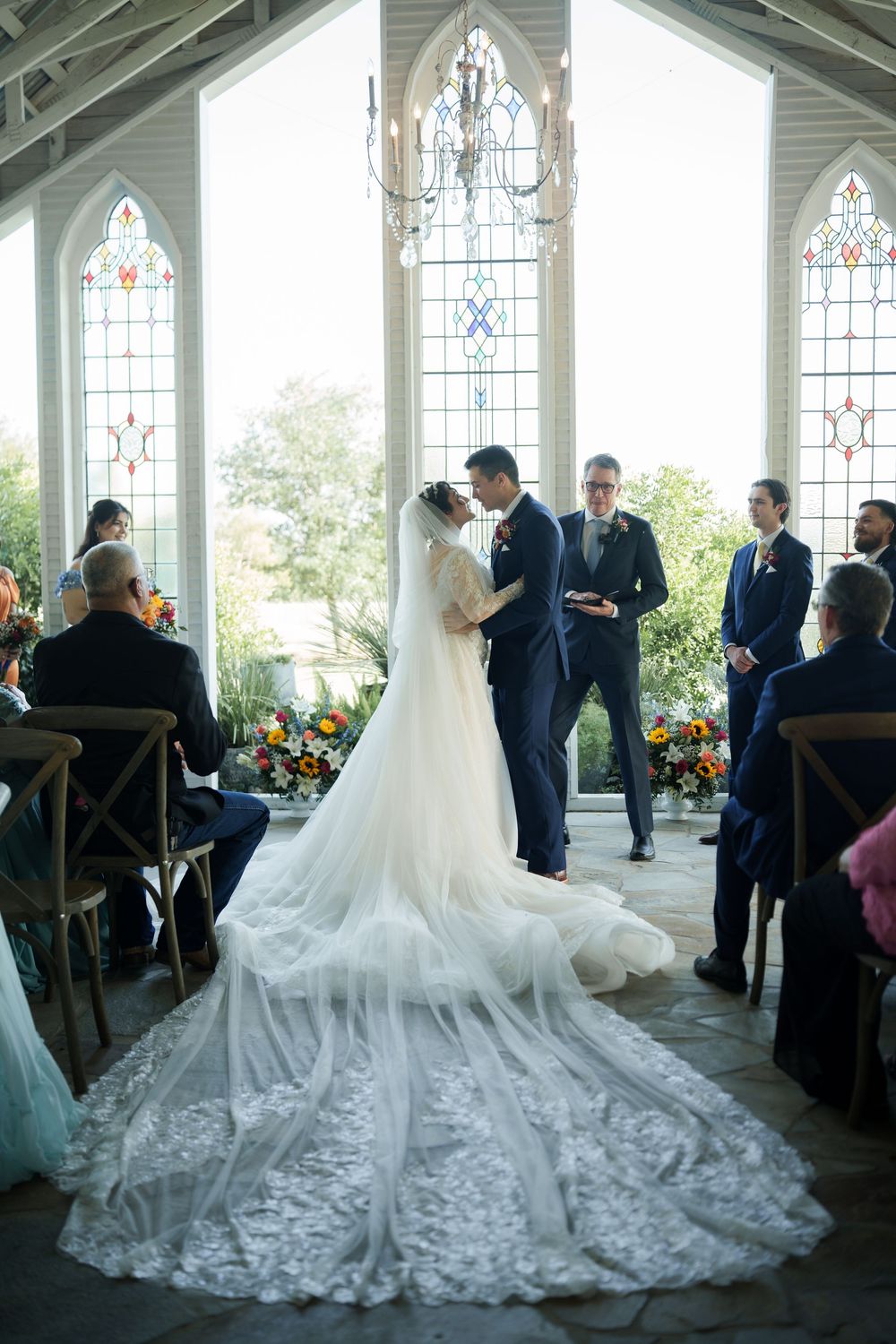 Couple exchanges vows in chapel with dramatic cathedral veil and stained glass windows.
