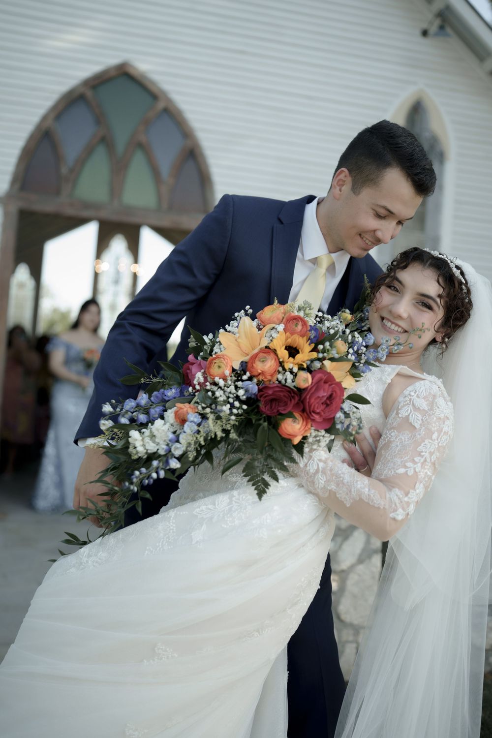 Joyful wedding portrait with colorful bouquet outside chapel entrance.