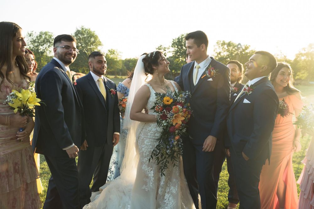 Wedding celebration outdoors with bridal party holding colorful bouquets at golden hour.