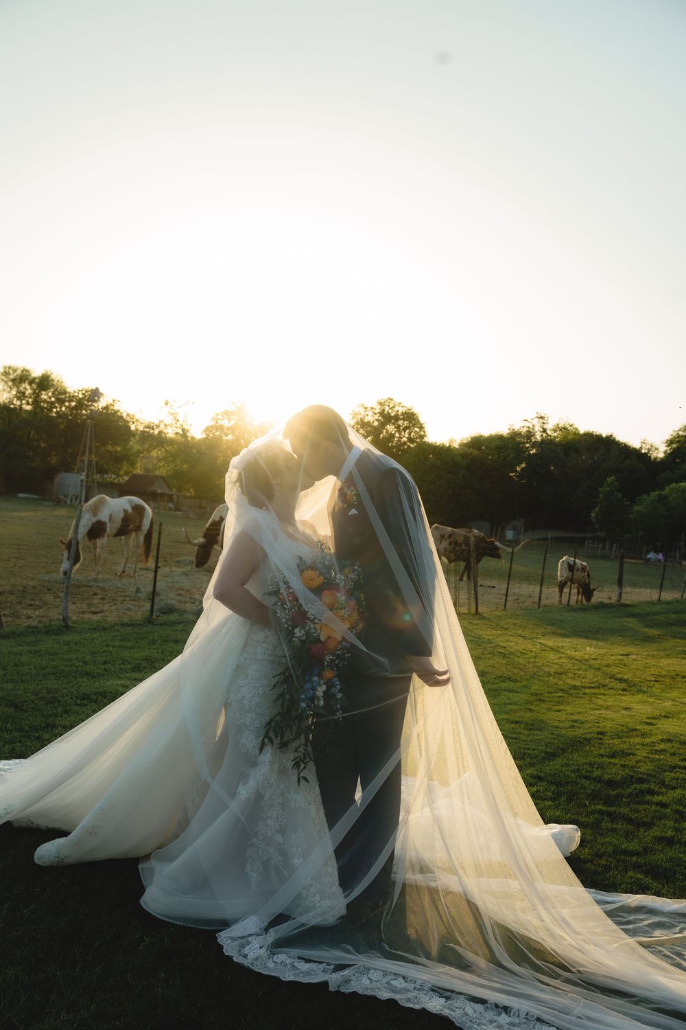 Elegant wedding dress with long train photographed in golden sunlight on grassy field.
