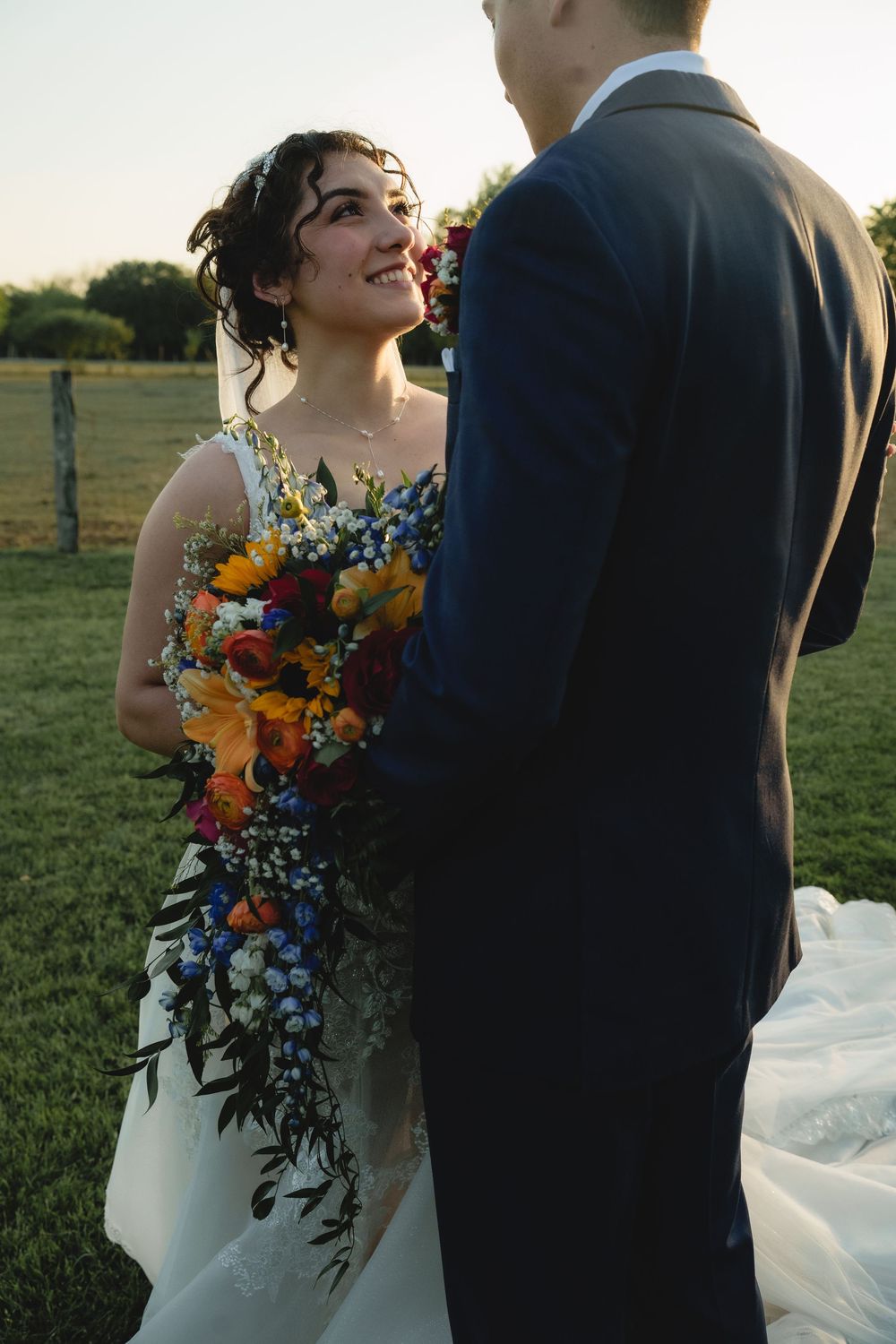 Wedding couple poses with vibrant sunflower bouquet against natural outdoor backdrop.