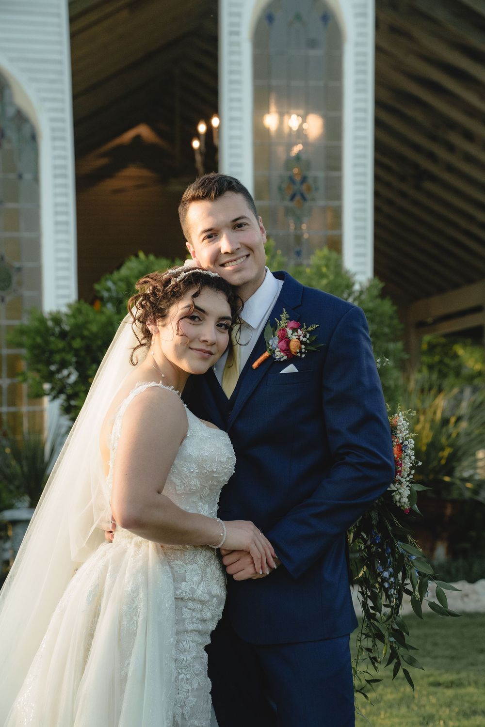 Wedding couple poses in elegant attire against white architectural backdrop.
