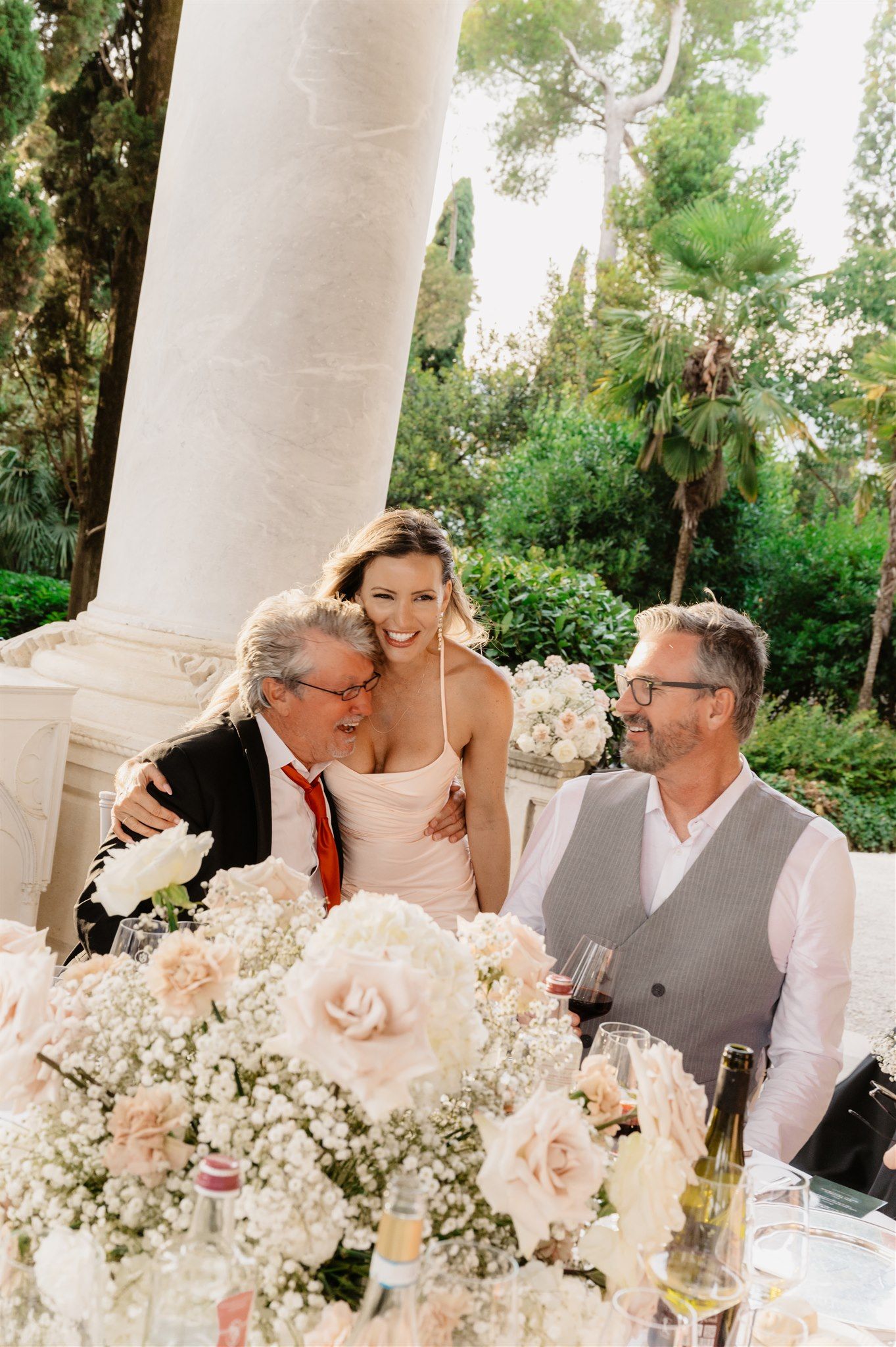 Outdoor wedding reception with guests seated at tables adorned with white floral centerpieces.
