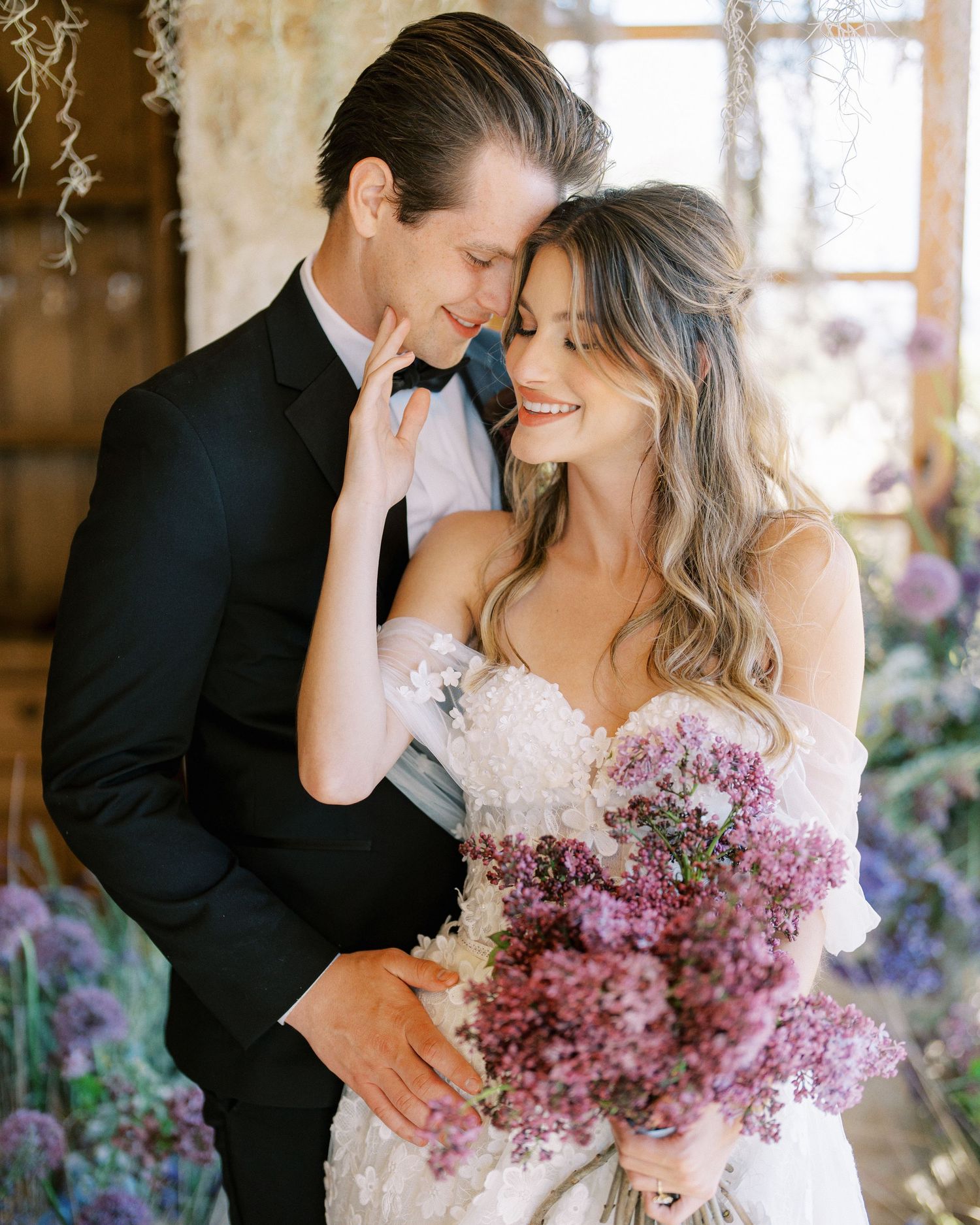 A romantic wedding moment with purple flowers and elegant attire in soft lighting.