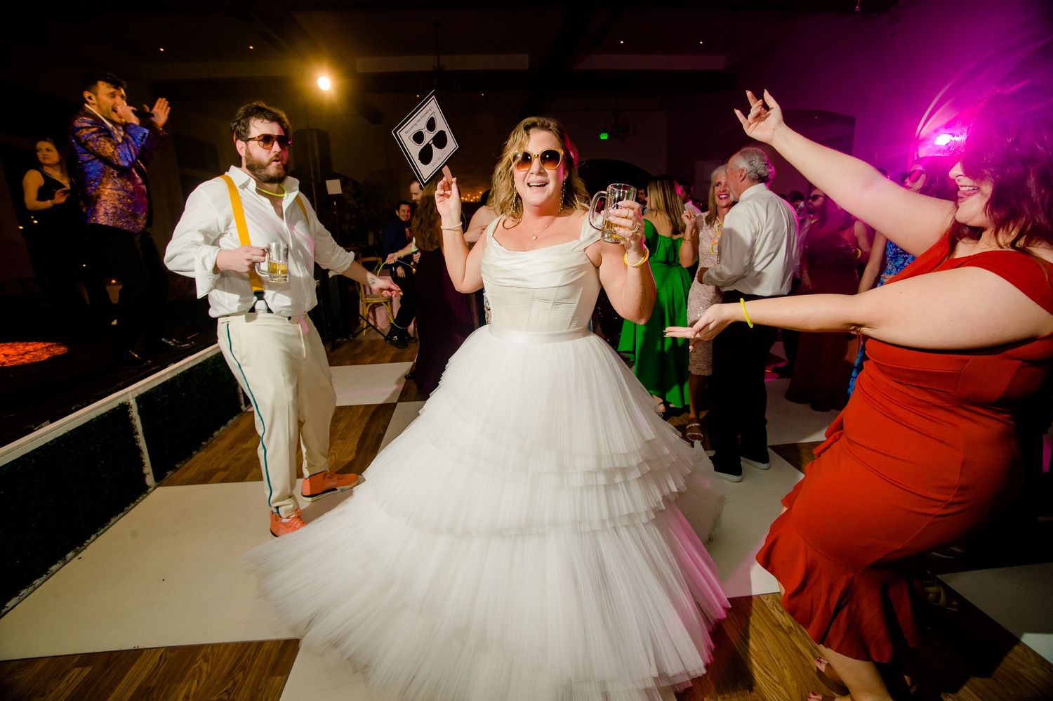 People dancing at a wedding reception on a white dance floor with purple and gold lighting in the background.