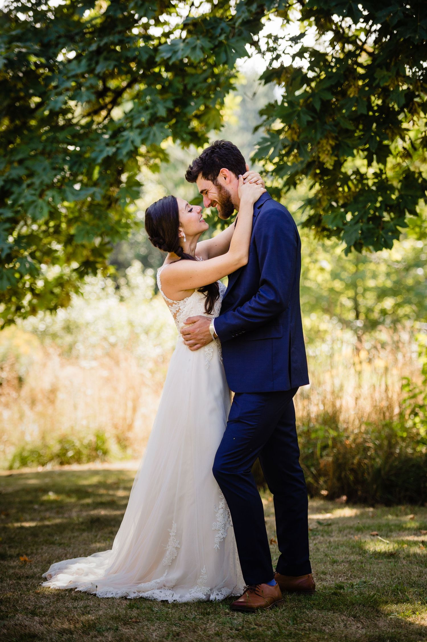 A newlywed couple shares romantic moments in a garden setting with sunlit trees and golden grasses in the background.