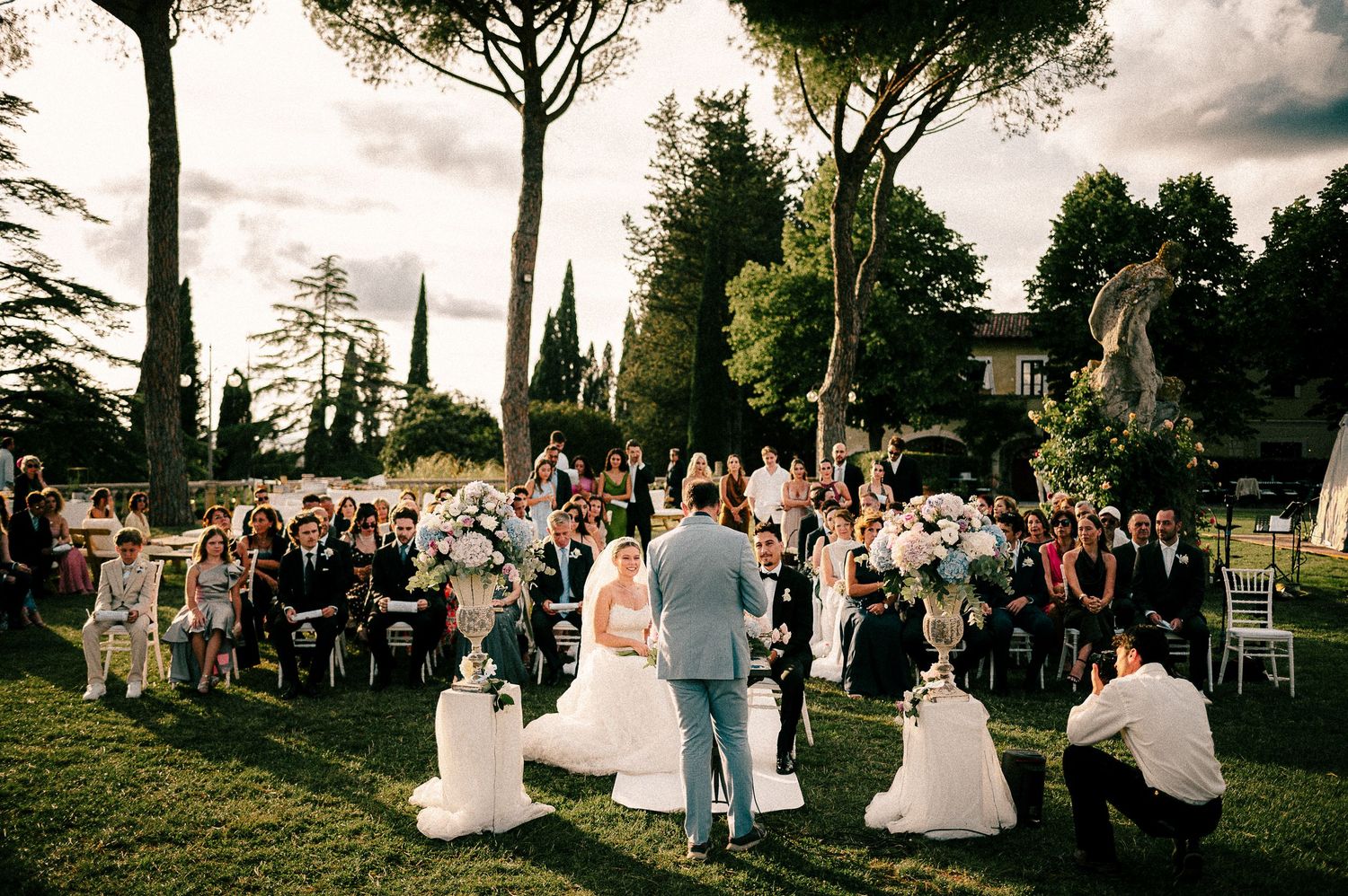 A crowd of formally dressed people dancing together at an evening wedding reception with streaked lights in background.