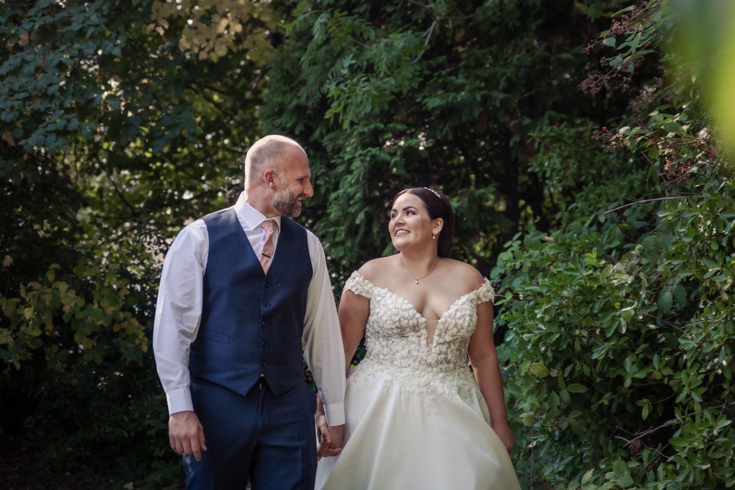 Couple in wedding attire walking together through garden setting.