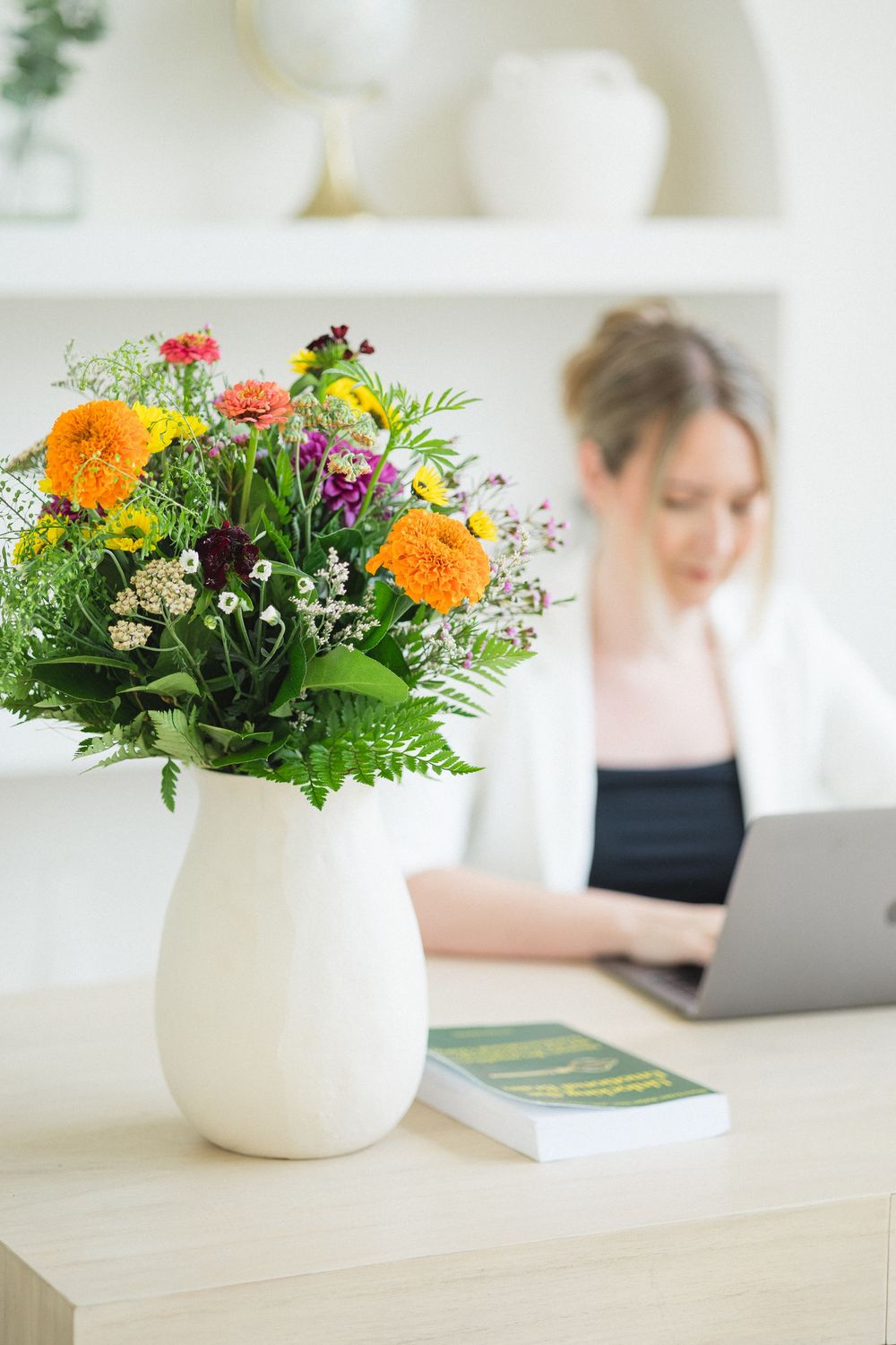 detail shot of colourful flowers in a white vase with an Ontario therapist working on her laptop in the background