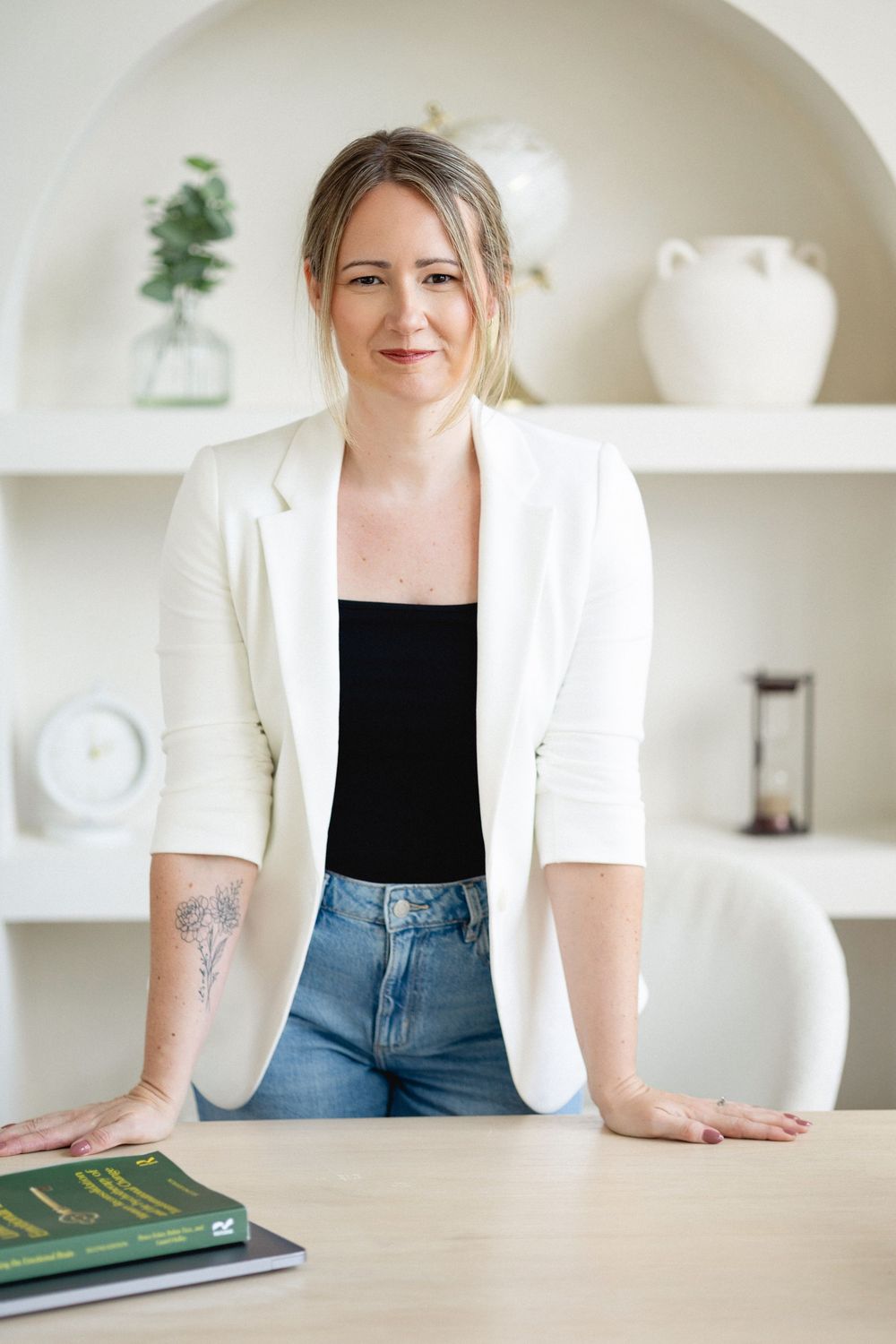 Strathroy virtual therapist with white blazer and hair pulled back leaning on desk during a personal branding session with captured by Thea