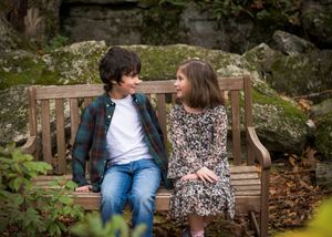 A couple sitting together on a wooden garden bench surrounded by lush greenery and natural scenery.