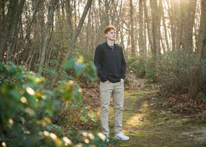 Person walking through sunlit forest path surrounded by trees and dappled golden light filtering through leaves.