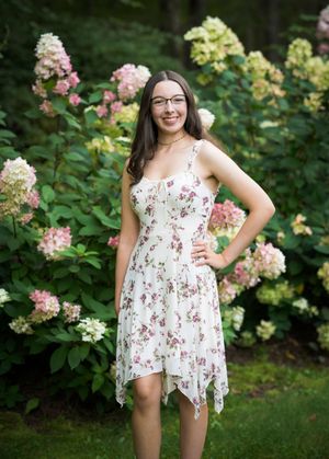 A summery floral print dress is worn in a garden setting with blooming hydrangea bushes in pink and yellow.