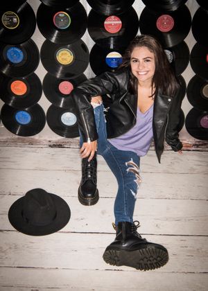 Stylish fashion shot against vinyl record wall backdrop with leather jacket, ripped jeans and combat boots on white wood floor.