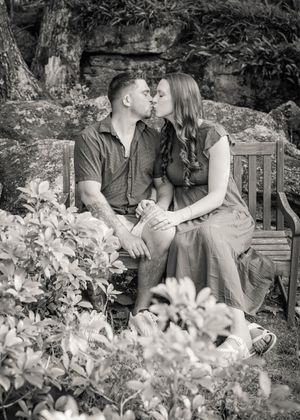 Romantic black and white portrait of a couple sharing an intimate moment on a garden bench surrounded by flowers.