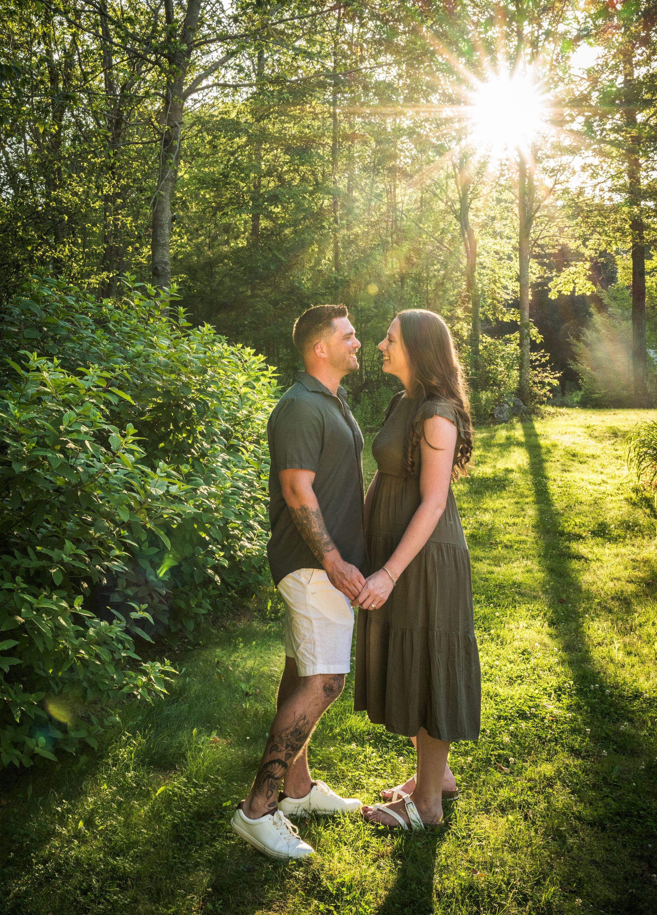 Two people share a romantic moment in a sunlit forest garden with golden rays streaming through the trees.