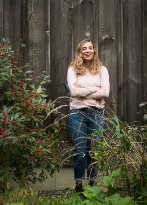 Person in a beige sweater stands against a rustic wooden fence with red berries and greenery in the garden.