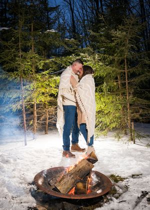 A couple shares a romantic moment by a campfire in the snowy woods on a winter evening.