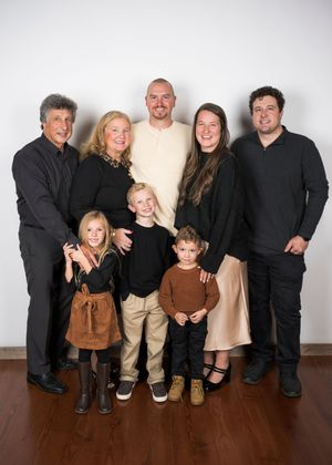 Multi-generational family portrait with seven people wearing casual attire against a light background.