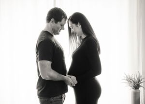 A black and white intimate moment between two people, with one gently touching a pregnant belly.